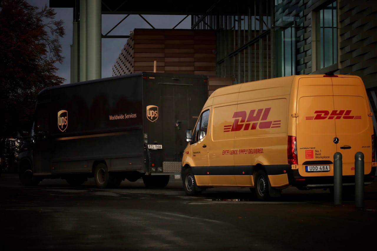 services-02 DHL and UPS delivery trucks parked at night near a modern building, ready for logistics operations.