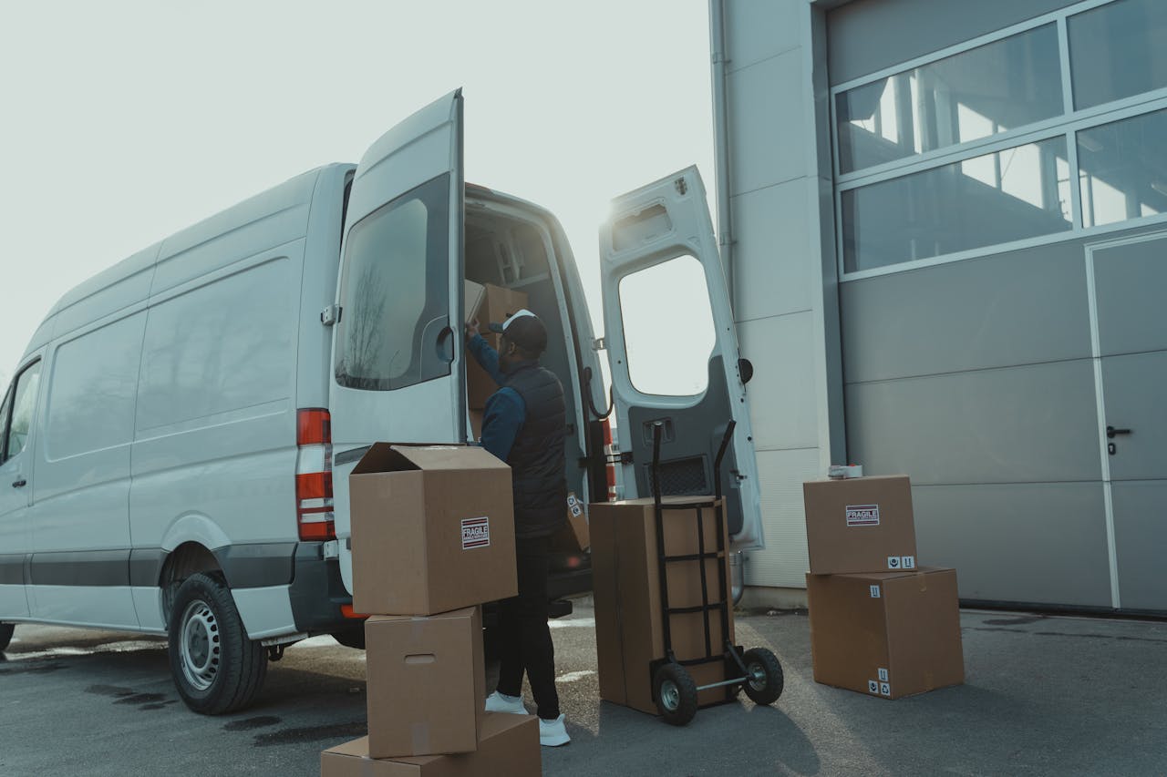 services-03 Courier loading cardboard boxes into a delivery van outside a warehouse.